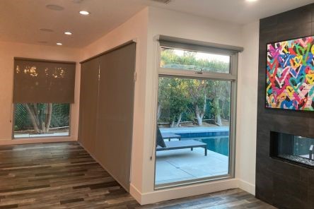 Light-filled Long Beach living room with custom sheer window shades partially down, revealing a beautiful backyard pool and patio.